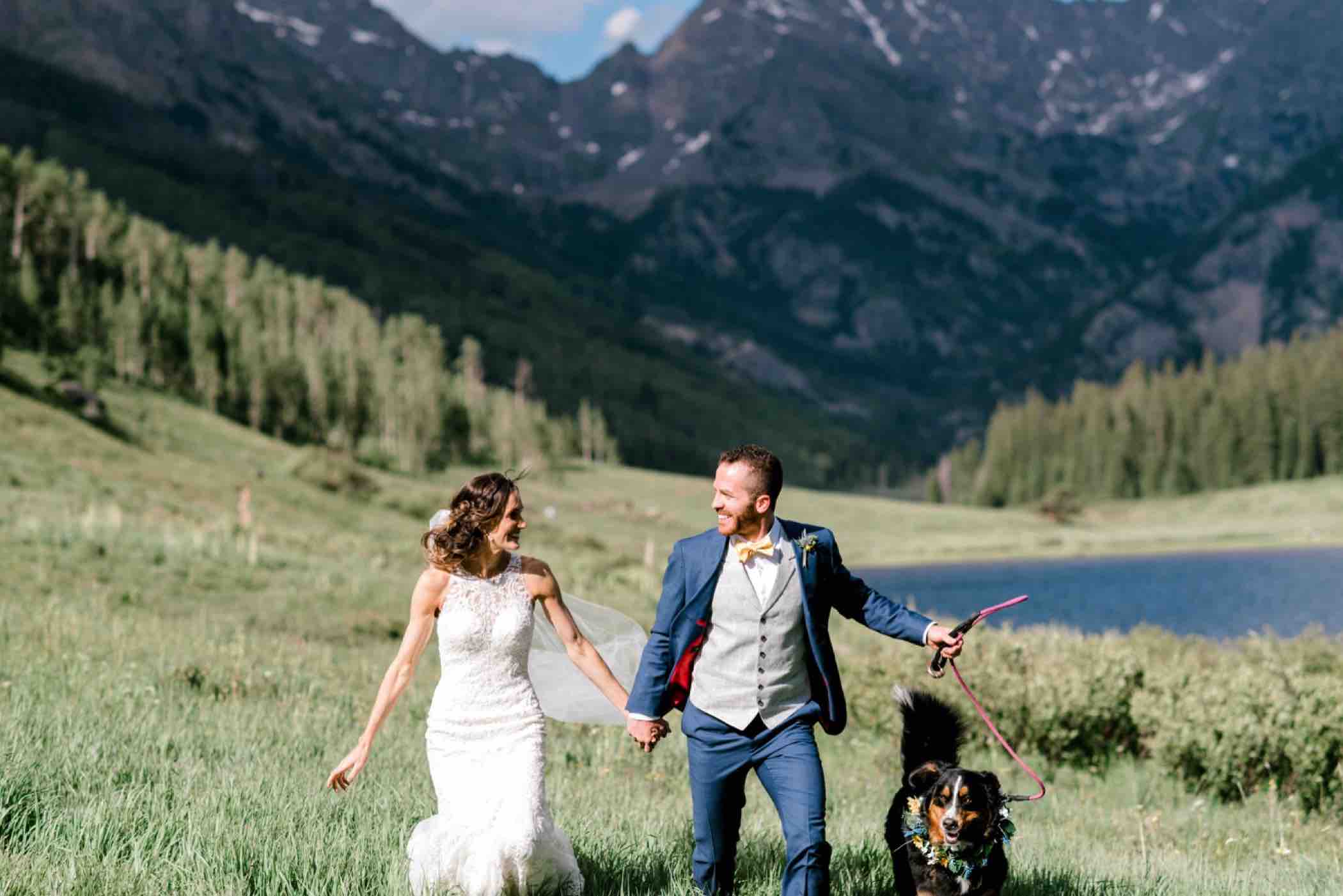Bride and groom walk with their Bernese Mountain dog Lucie following their wedding ceremony at Piney River Ranch. The Rocky Mountains are visible behind them. Photo by Ali and Garrett, Romantic, Adventurous, Nostalgic Wedding Photographers.