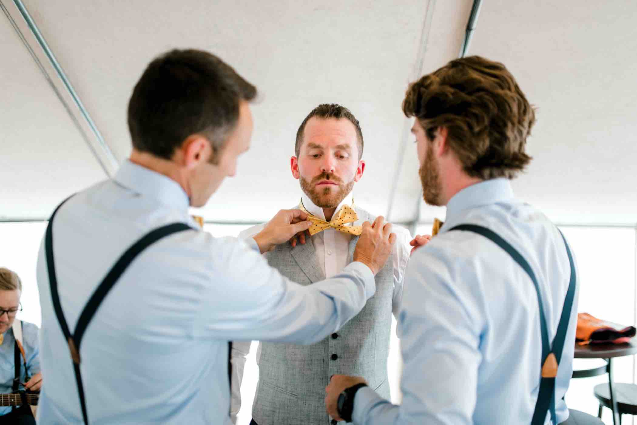 Kris' groomsmen help him adjust his yellow spotted bowtie before his wedding at Piney River Ranch in Vail, Colorado. Photo by Ali and Garrett, Romantic, Adventurous, Nostalgic Wedding Photographers.