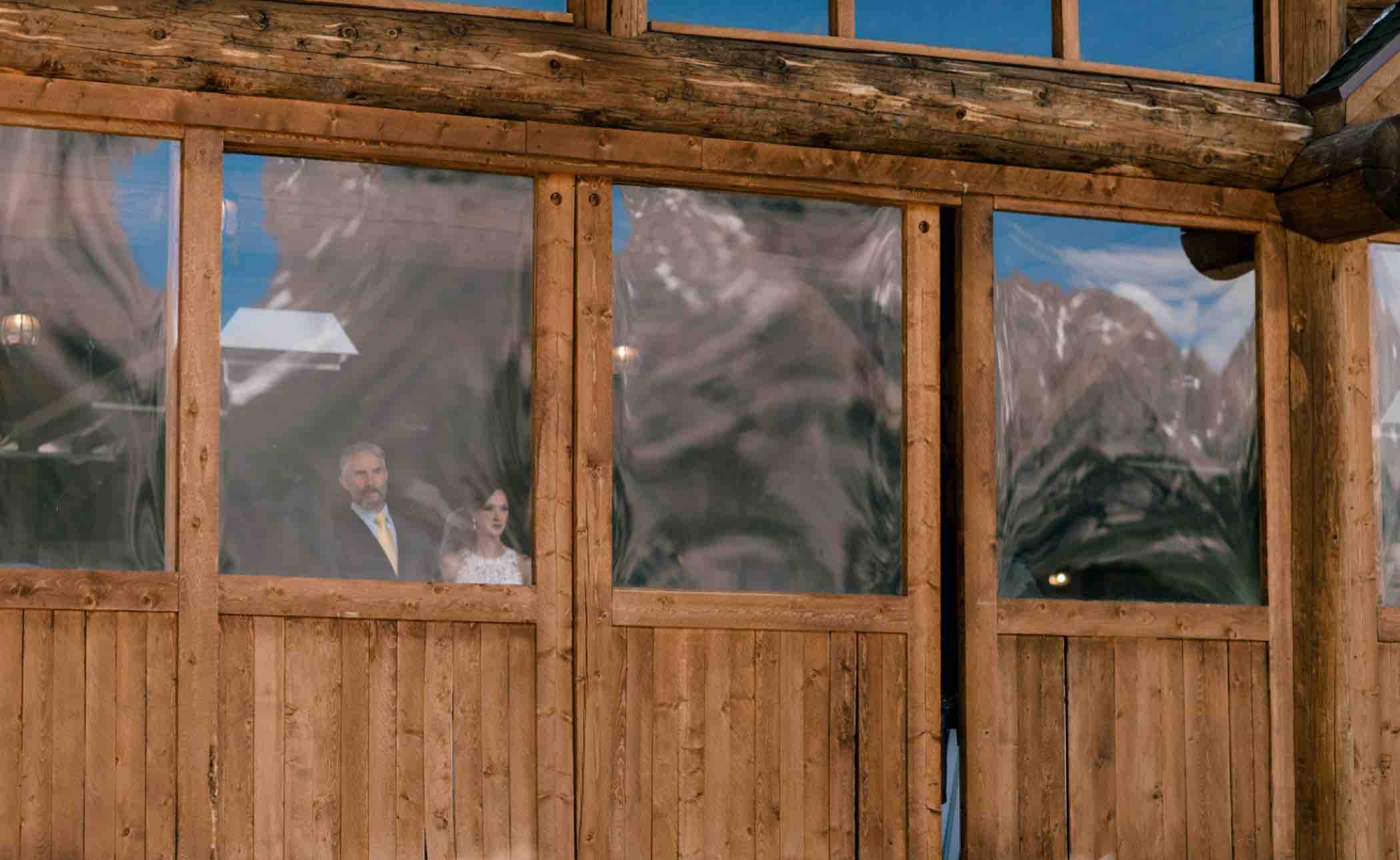 Sallie, the bride, can be seen in the windows of the Piney River Ranch in Vail in the Colorado Rocky Mountains. Photo by Ali and Garrett, Romantic, Adventurous, Nostalgic Wedding Photographers.