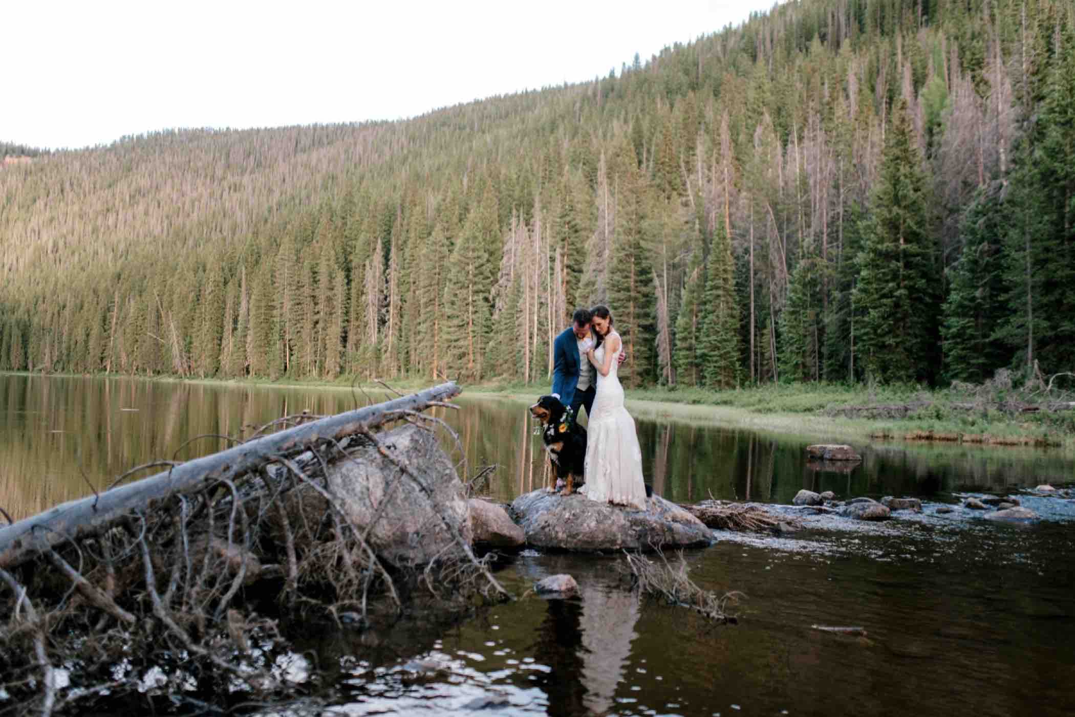 Bride and groom stand in the water with their Bernese Mountain Dog of Piney Lake at Piney River Ranch in Vail, Colorado. Photo by Ali and Garrett, Romantic, Adventurous, Nostalgic Wedding Photographers.