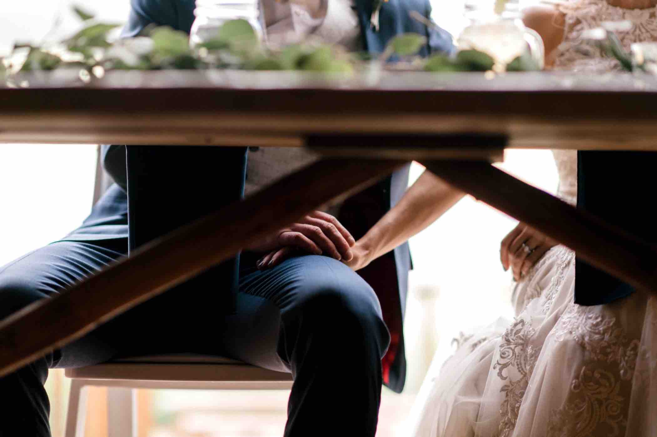Bride and groom hold hands under the table during an intimate moment at their wedding reception at Piney River Ranch in Vail, Colorado. Photo by Ali and Garrett, Romantic, Adventurous, Nostalgic Wedding Photographers.