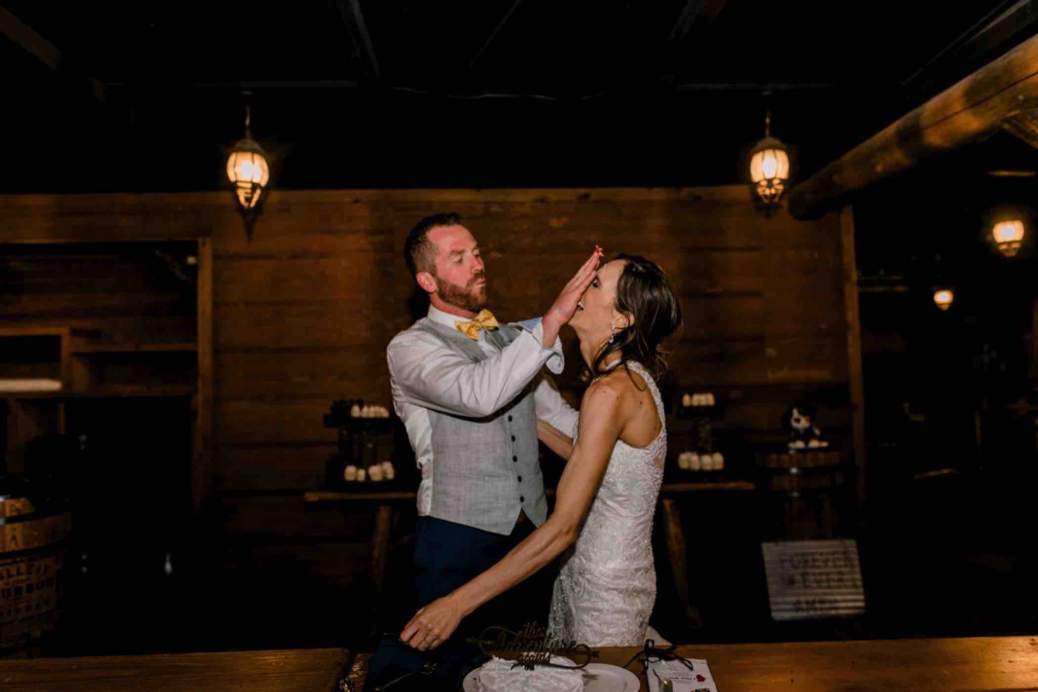 The groom smashes the cake onto his bride's face during their wedding reception at Piney River Ranch in Vail, Colorado. Photo by Ali and Garrett, Romantic, Adventurous, Nostalgic Wedding Photographers.