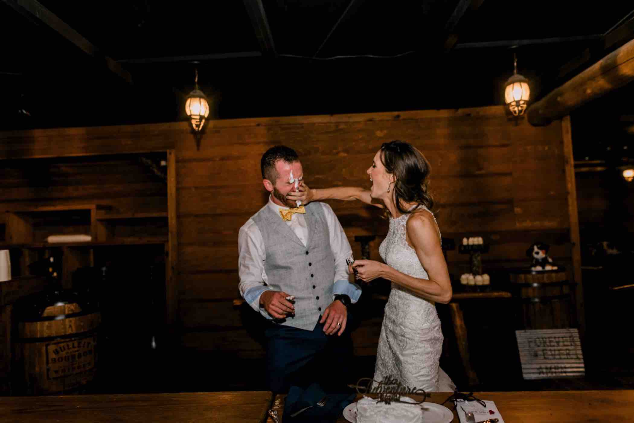 The bride smears cake on the groom during their wedding reception at Piney River Ranch in Vail in the Colorado Rocky Mountains. Photo by Ali and Garrett, Romantic, Adventurous, Nostalgic Wedding Photographers.